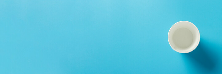 Empty paper cup for drinks on a blue background. Banner. Flat lay, top view