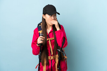 Young Chinese girl with backpack and trekking poles over isolated blue background doing surprise gesture while looking to the side