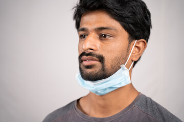 concept showing of improper way of using face masks during coronavirus or covid-19 crisis - young man wearing medical at neck on isolated background