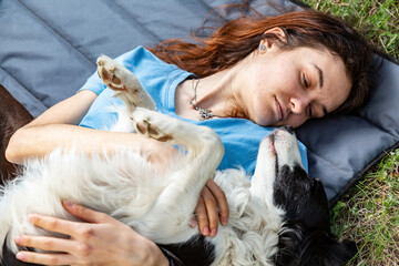 A girl lies in a clearing with a border collie dog and look at each other. Horizontal orientation.