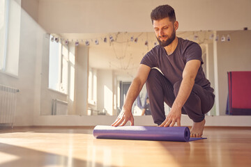 Handsome young man rolling yoga mat in fitness studio