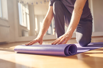 Young man rolling yoga mat in fitness studio