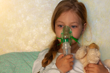 Little girl making inhalation with nebulizer on a bed at home. Sick allergic kid asthma inhaler...
