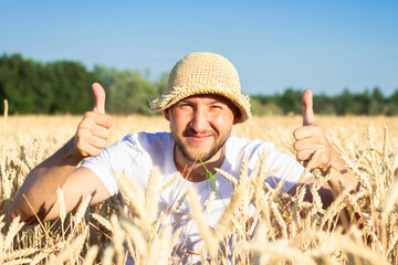 Young man in a hat peeks out of wheat, a field of wheat. Happy farmer concept, good harvest