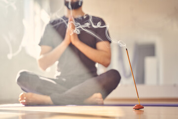 Young man practicing yoga in studio with incense stick - obrazy, fototapety, plakaty