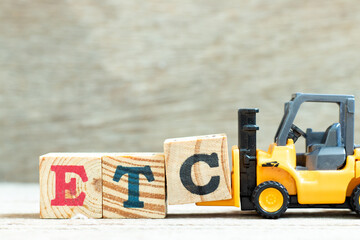 Toy forklift hold letter block c to complete word etc (abbreviation of et cetera) on wood background
