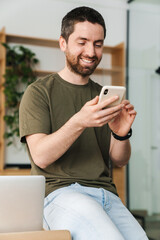 Photo of man smiling and using cellphone while sitting on table
