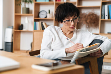 Image of concentrated woman making notes in diary while sitting