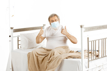 Elderly old man recovering in a hospital bed isolated on white background. Getting care and treatment. Concept of healthcare and medicine, diagnostics. Put on protective face mask. Copyspace.