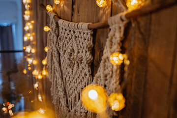 macrame hanging on a wooden wall surrounded by lights from a garland, muted light, photos with noises, blurred background