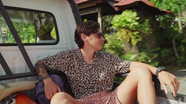 Handheld Shot Of Happy Young Man In Sunglasses Smiling And Riding In Back Of Pickup Truck While Vacationing In Bali