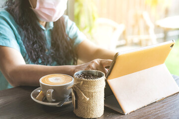 Quarantined woman work from home by using a tablet and stress relief with hot coffee. New normal lifestyle. Selective focus on right index finger.