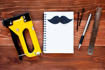 .open notebook with black mustache and tools on a brown wooden background. concept of shopping planning for repairs.