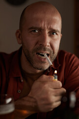 Portrait of balded mature man looking at camera while smoking the cigarette at the table