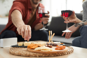 Close-up of wooden tray with different kinds of cheese on the table with couple drinking wine in the background