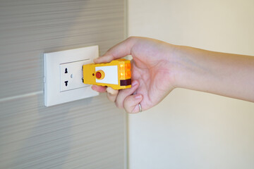 Hand holding electric tester for checking plug at the power outlet in on the wall. Check the...