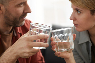 Close-up of young couple looking at each other and toasting with glasses of alcohol drinks