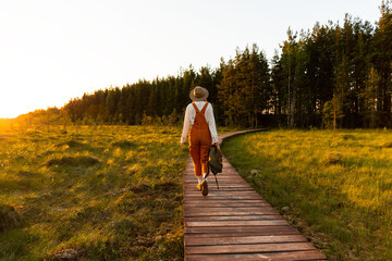 Woman botanist with backpack on ecological hiking trail in summer outdoors. Naturalist exploring...