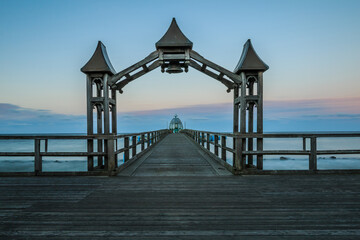 Pier on the Baltic Sea in the evening. Sunset with clouds on the horizon. Unlit wooden footbridge with wooden arch and bell on the island of Ruegen