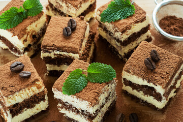 Pieces of tiramisu cake with delicate cream, coffee beans and mint leaves.