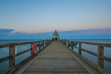 Obraz premium Pier on the Baltic Sea in the evening. Wooden jetty with a lifebuoy on the site and diving bell at the end. Evening horizon with clouds and calm sea on the island of Ruegen