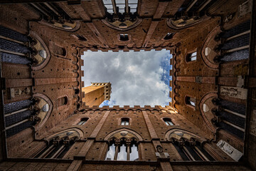 wide angle view from inner courtyard of old medieval brick tower, Torre del Mangia tower at Palazzo Pubblico in Siena, Tuscany region, Italy