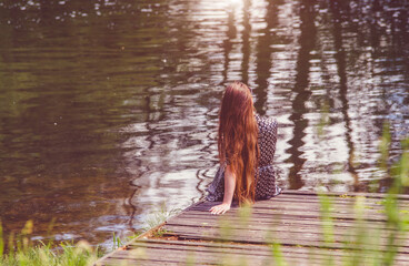 The girl is sitting on a wooden platform near the lake
