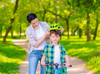 A young mother puts a bicycle helmet on to her son. Safe riding a bike concept