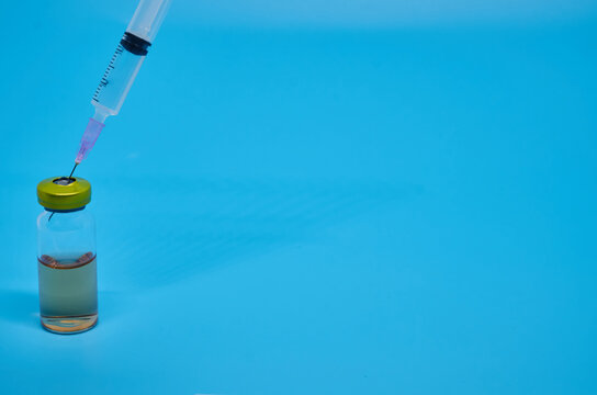 syringe with vial and orange liquid in flask with chemical structure background in blue science laboratory