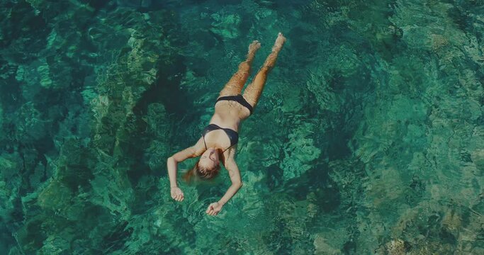 Aerial view of beautiful young woman relaxing, floating in the ocean, spa wellness lifestyle