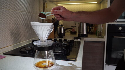 Drip coffee, pouring water over roasted.Man pouring water from the kettle into the coffee filter. Fresh morning pour over coffee blossoms in the dripper.