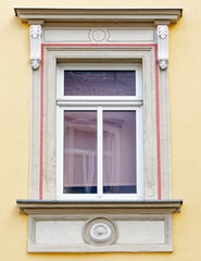 vintage decorated window frame with red stripe on light ocher house wall