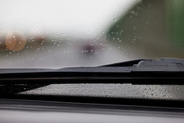 Fragment mokrej od deszczu szyby w samochodzie wraz z wycieraczką, widok z wnętrza auta. Rozmyte tło.