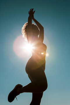 Young female dancer dances at sunset wearing sportswear . Silhouette backlight of the sun with body movements. Freedom and happiness concept.