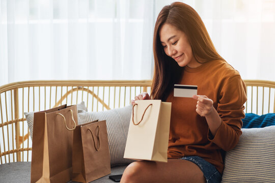 Closeup image of a beautiful young woman holding credit card while opening shopping bags at home