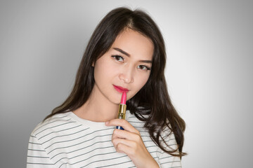 Beautiful Asian young brunette girl with curly hair applying pink lipstick on white background