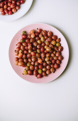 Fresh ripe gooseberries in a pink plate on a white table, healthy food.