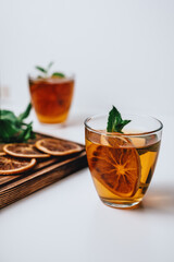 Golden drink, iced tea with a ring of dried orange and mint on a white background.
