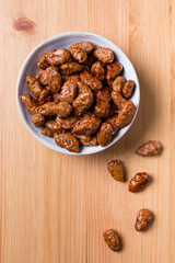 Amêndoas caramelizadas em um pote de cerâmica sobre mesa de madeira vista de topo