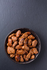 Amêndoas caramelizadas em pote de ceramica sobre pedra de ardósia escura vista de topo