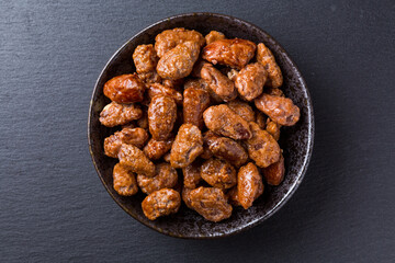 Amêndoas caramelizadas em pote de ceramica sobre pedra de ardósia escura vista de topo