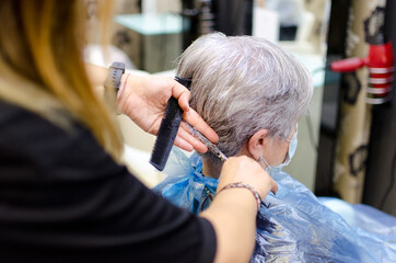 Anciana con cabello blanco cort&aacute;ndose el pelo en una peluquer&iacute;a con mascarilla