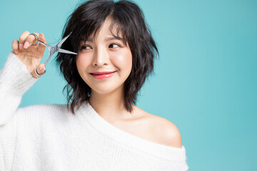 Young Asian woman cutting her bangs by herself isolated image on studio background