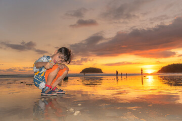Fototapeta na wymiar .A cute boy playing sand on Kata beach,Phuket at sunset time..