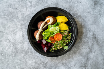 Healthy Vegan Take Away Falafel Bowl with Mung Bean Salad, Legume, Roasted Beet and Yellow Turmeric Hummus Tahini Sauce in Black Plastic Plate Cup Package / Container.