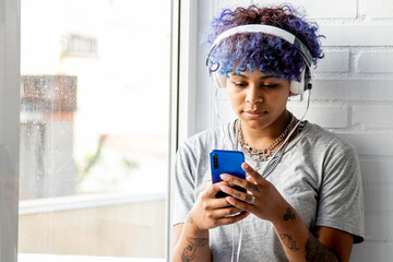 young woman afro american with headphones and mobile phone at the window