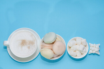 A cup of aromatic latte coffee and delicate vanilla marshmallows in small cups on a blue background. Place for text