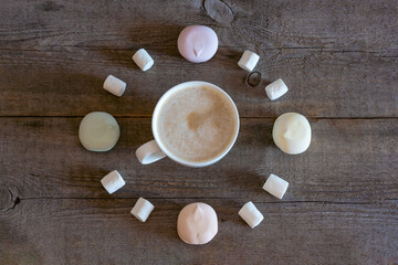 White cup of coffee, cocoa on a wooden background, marshmallows roll in the shape of a clock. Alarm concept.