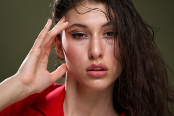 Naklejka premium A sensual young woman portrait in a red jacket, with wet long black hair poses against a green background in the studio.