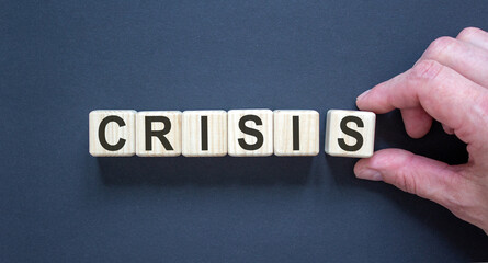 Wood cubes with word 'crisis' on paper black background, copy space. Male hand. Business concept success process.